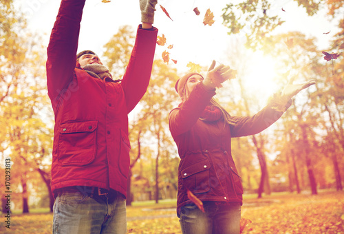 happy young couple throwing autumn leaves in park