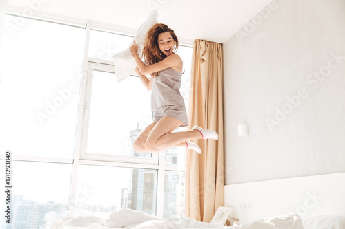 Happy pretty lady jumping on bed holding pillow