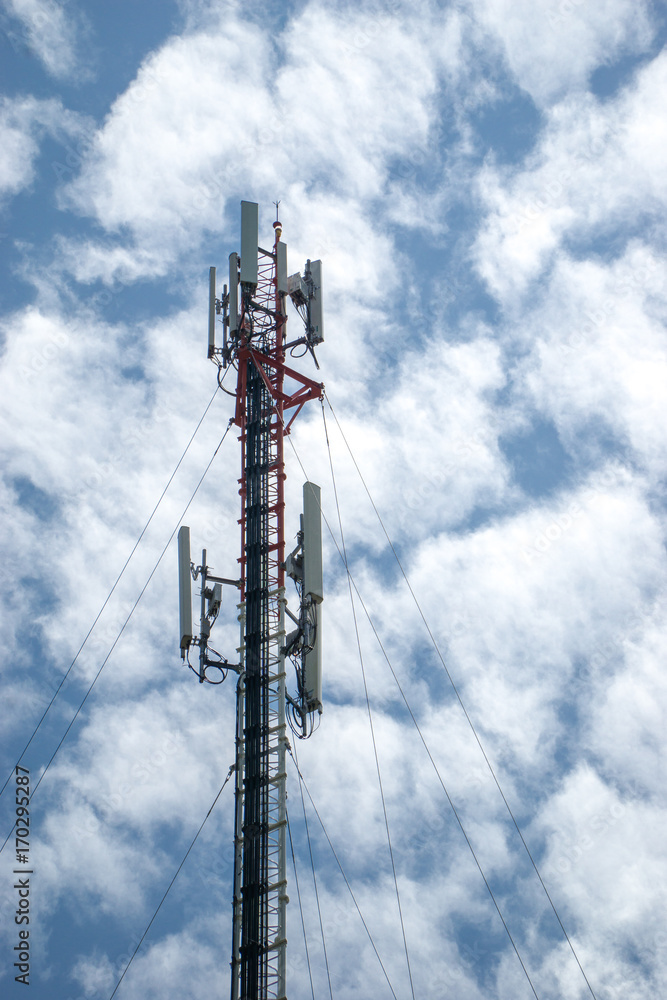 Mobile phone and communications tower with cloud and blue sky.