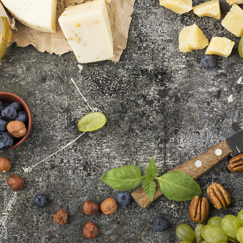 Young white cheese, a new recipe for cheese with fenugreek, a hard chopped Parmesan on a gray stone background with blueberries, nuts, green grapes, honey. Top view. Selective focus.. photo