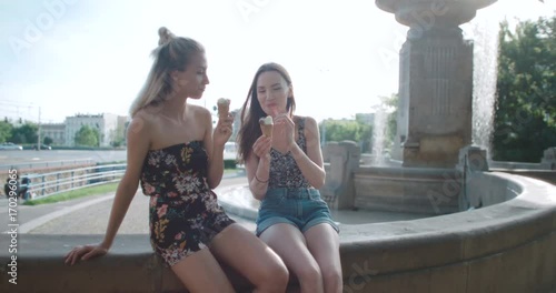 Two female friends eating ice cream and chatting in a city. 