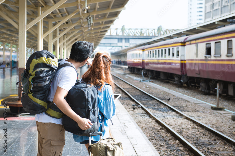 Naklejka premium Couple traveler searching right direction at train station.Asian Backpackers pointing and planning holiday vacation with gps map in tablet.Travel concept.