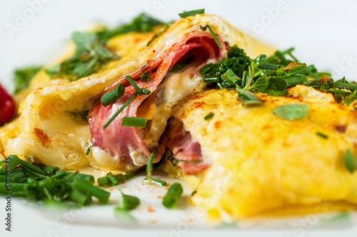 Fluffy stuffed egg omelette with ham, cheese and green herb, closeup.