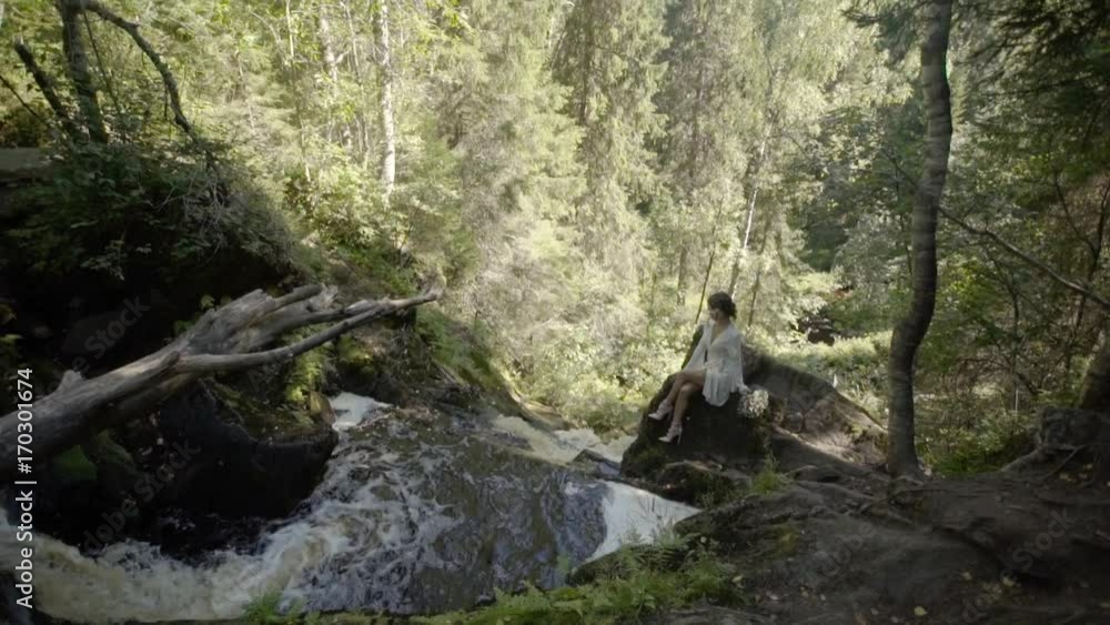Young woman sitting on a rock near waterfall in lingerie Young woman sitting on a rock near waterfall in lingerie