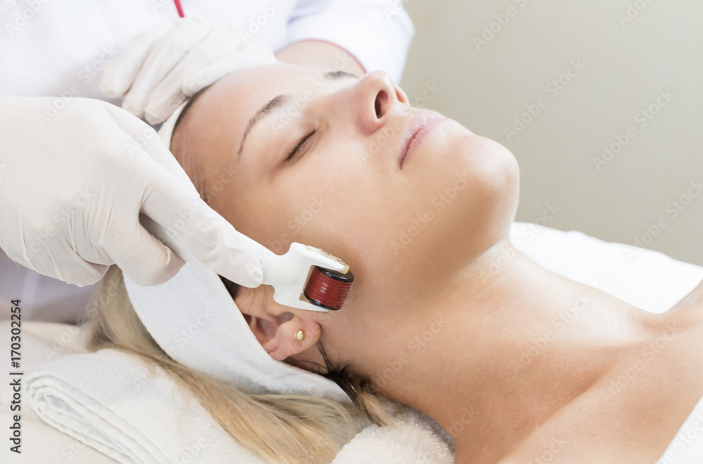 The woman undergoes the procedure of medical micro needle therapy with a modern medical instrument derma roller. 