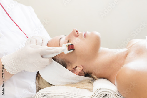 The woman undergoes the procedure of medical micro needle therapy with a modern medical instrument derma roller.  photo