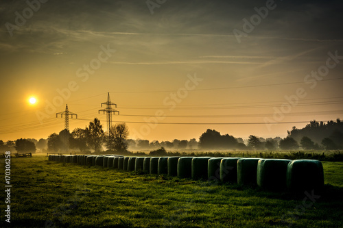 Sunrise in foggy fields with hay bales photo