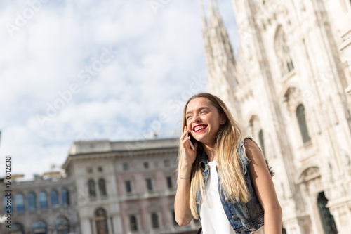 Pretty and happy blonde teenager outdoor talking on her mobile phone. Photo taken in Milan, Italy.