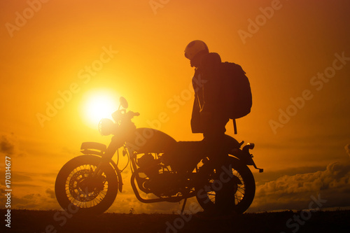 Fotografie Silhouette of biker man  with his motorbike,he shoulder backpack