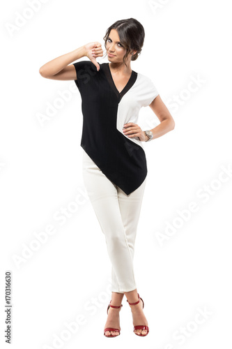 Smiling young business woman showing thumb down hand sign looking at camera. Full body length portrait isolated on white studio background