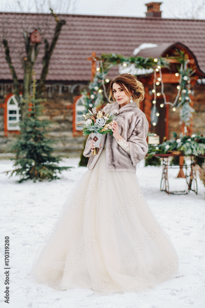 Portrait of a beautiful bride holding a wedding bouquet outdoors in a winter park.