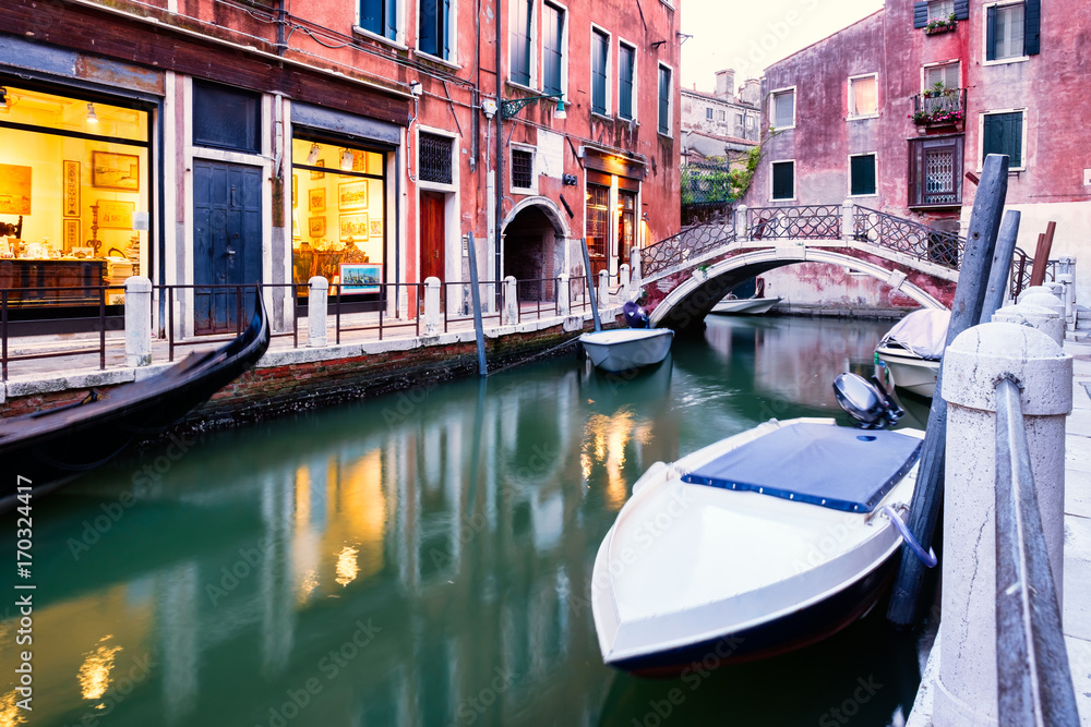Boats and old houses on a narrow canal in Venice at sunset