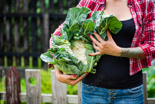 Tatooed millennials girl holding cauliflower in garden
