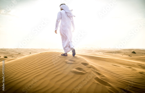 Arabic man with traditional emirates clothes walking in the desert