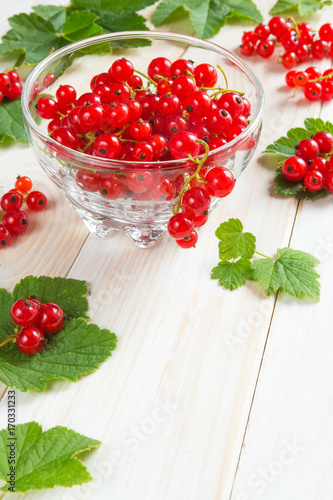 Berries of a red currant in a glass bowl pattern and background of branches of berries and leaves on a light wooden table rural style with copy space, concept of eco nutrition and vegetarianism
