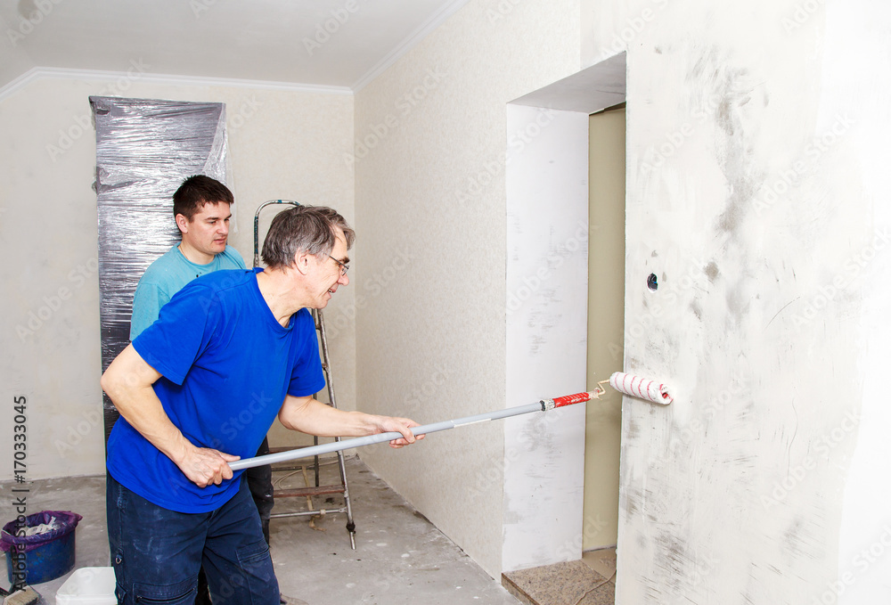 worker painting wall with background glue for a wallpaper worker painting wall with background glue for a wallpaper