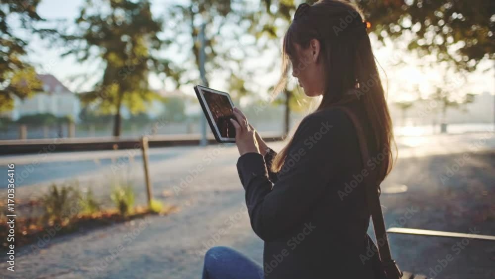 Young Businesswoman Using Digital Tablet, Sitting on the Bench in the Park in the Sunny Morning City. SLOW MOTION. STEADICAM Stabilized Shot. Business Woman Relaxing Outdoors. Lens Flare. Young Businesswoman Using Digital Tablet, Sitting on the Bench in the Park in the Sunny Morning City. SLOW MOTION. STEADICAM Stabilized Shot. Business Woman Relaxing Outdoors. Lens Flare.