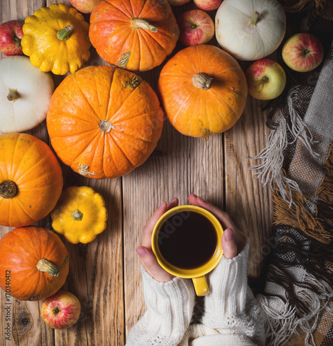 Hands keeping cup of coffee and pumpkins on wood background