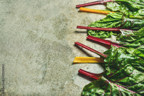 Flat-lay of fresh leaves of swiss chard over grey concrete stone background, copy space, selective focus. Food frame. Clean eating, vegetarian, alcaline diet, organic, healthy cooking concept