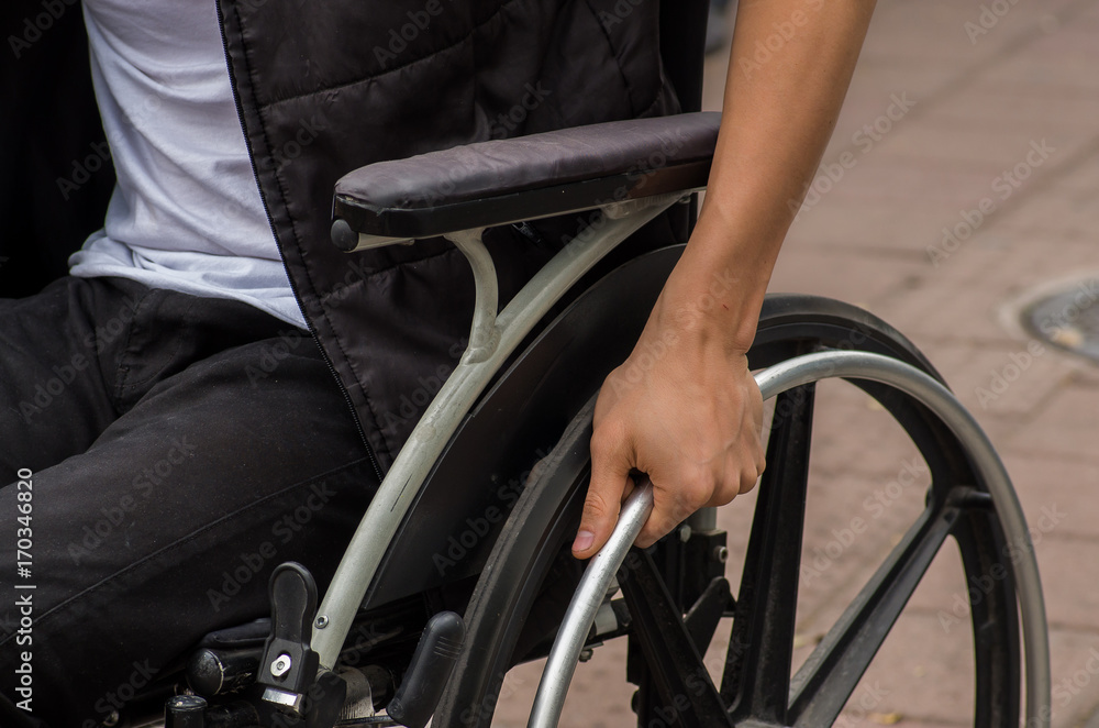 Obraz premium Close-up of male hand on wheel of wheelchair during walk in park