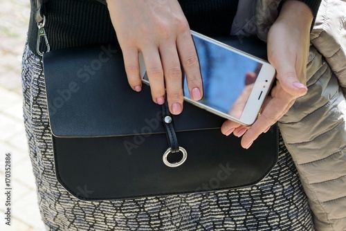 смартфон в руках девушки и чёрная сумка