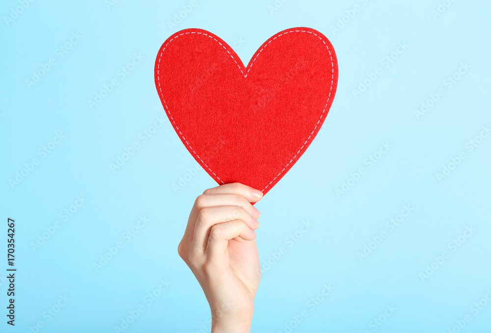 Woman holding red heart on color background. Volunteer concept