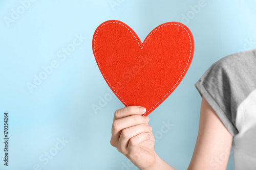 Woman holding red heart on color background. Volunteer concept