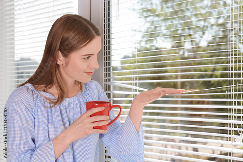 Beautiful young girl looking in window and holding cup of coffee or tea in hand