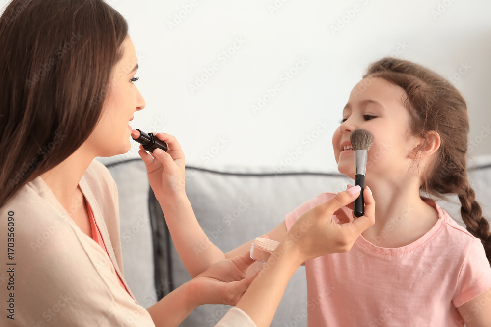 Young woman and her little daughter applying makeup at home Young woman and her little daughter applying makeup at home