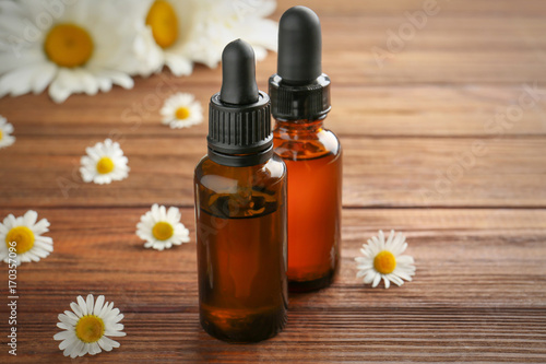 Two bottles of essential oil with fresh chamomiles on table