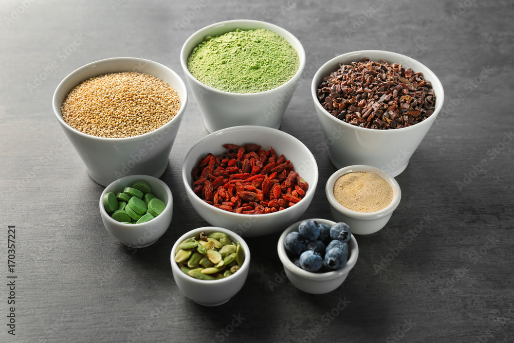 Composition with assortment of superfood products in bowls on grey table