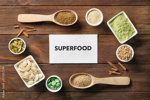 Composition with paper card and assortment of superfood products on wooden background