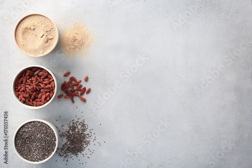 Composition with assortment of superfood products in bowls on light textured background, top view