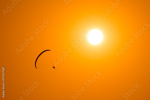 Paraglider flies in the sky with sun on the background