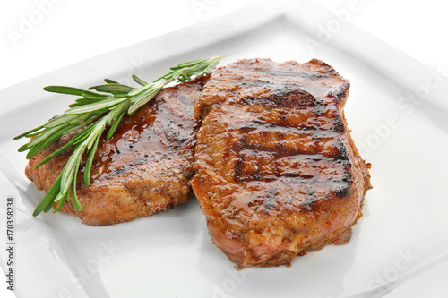Plate with tasty steaks on white background