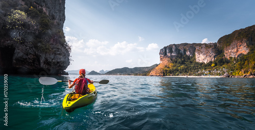 Woman paddles kayak in the calm sea among the tropical islands