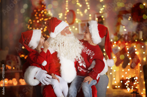 Cute little boy and girl with Santa Claus in room decorated for Christmas