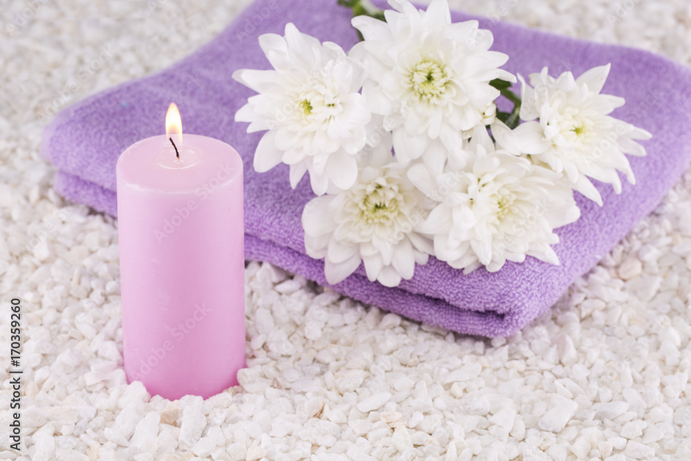 Spa. Still life. Candle of pink color, a towel and white flowers on a background of white pebbles.