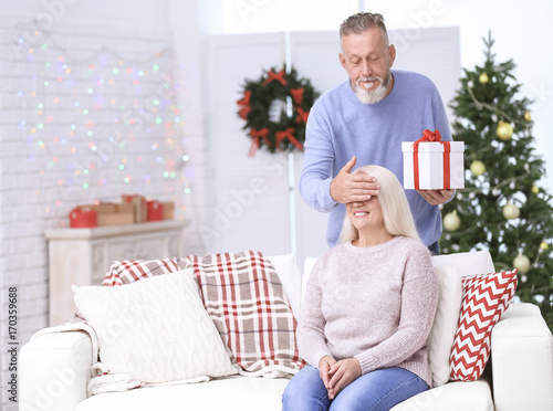 Senior man giving Christmas present to his wife at home