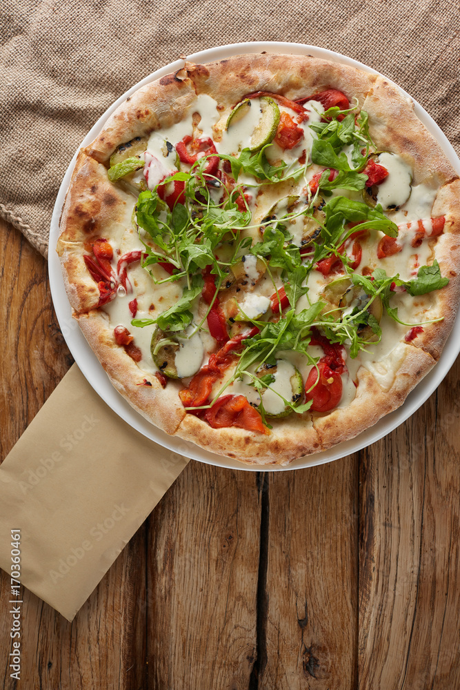 Rounded homemade pizza with paprika, basil, cheese at wooden background.