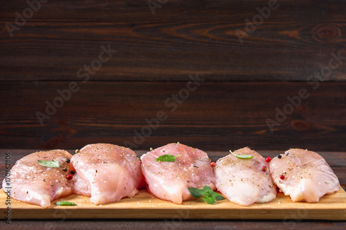 Raw chicken fillets on a cutting board against the background of a wooden table. Meat ingredients for cooking. Empty place for an inscription. Copy the space.