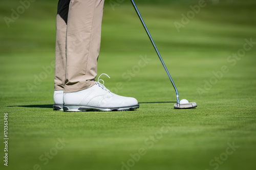 Close up of a male golf player with white shoes putting on green