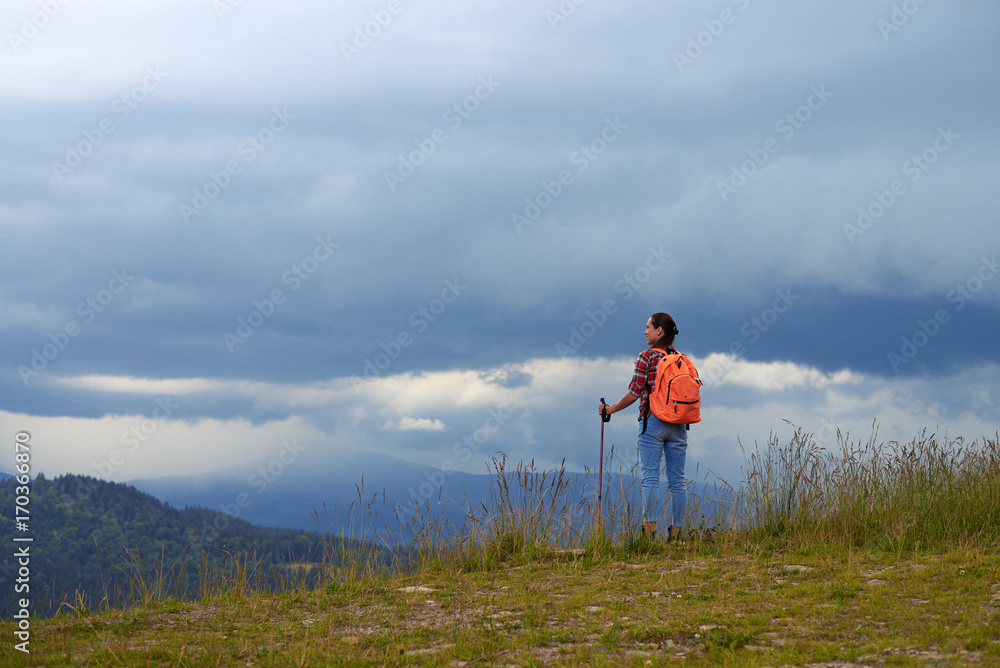 Mid shot of cheerful female standing on mountain with hiking poles