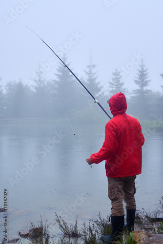 Man in waterproof jacket fishing on rainy weather