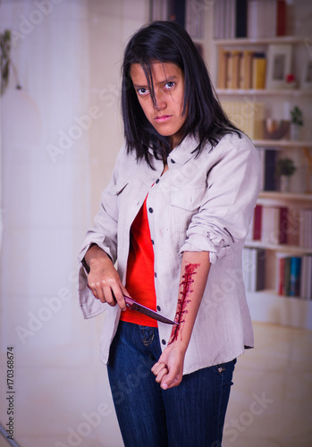 Close up of a young depressive teenager holding a knife with her arm bleeding, in a blurred background photo