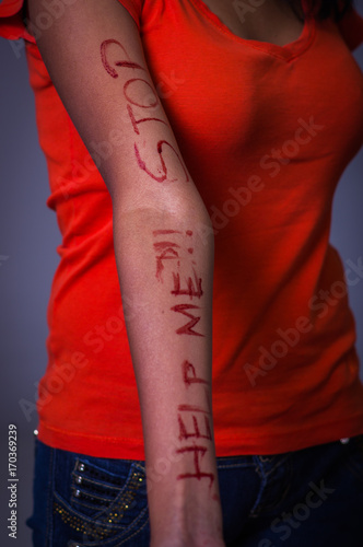 Close up of a young depressive woman, with her arm bleeding with the help me and stop words written in her arm with a knife, in a blurred background photo