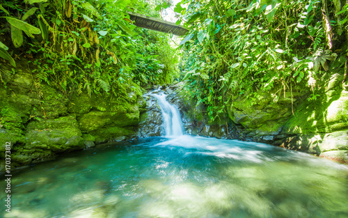 Beautiful small waterfall located inside of a green forest with stones in river at Mindo