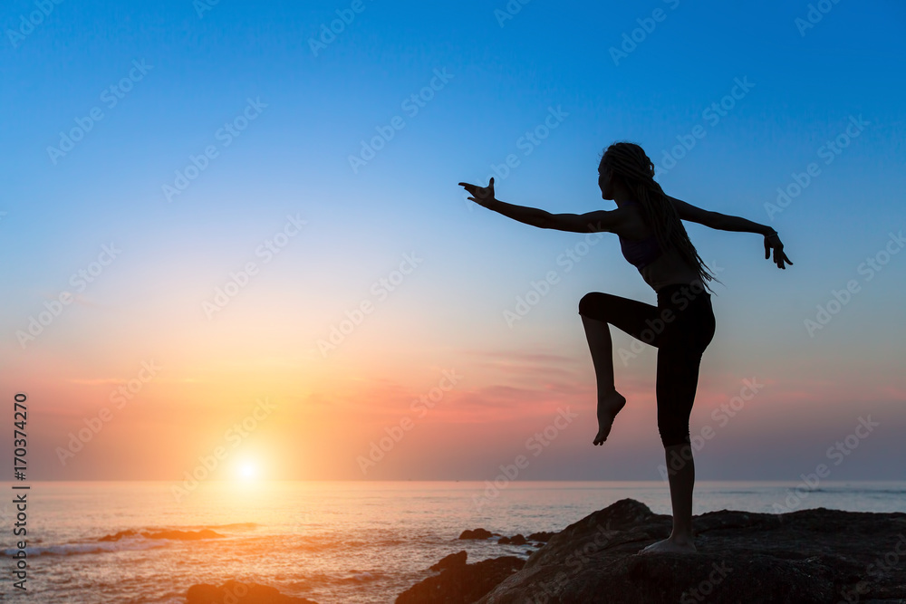 Silhouette flexible girl moves in a dance on the shore of the sea during twilight.