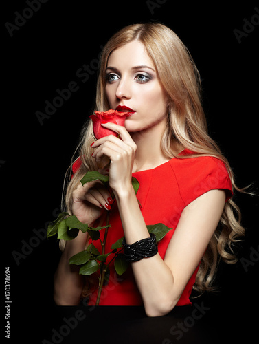 Portrait of young beautiful blonde woman in red dress with red rose in hands on black