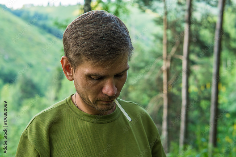 Young man is smoking cigarettes in a summer forest in the mountains. Young man is smoking cigarettes in a summer forest in the mountains.
